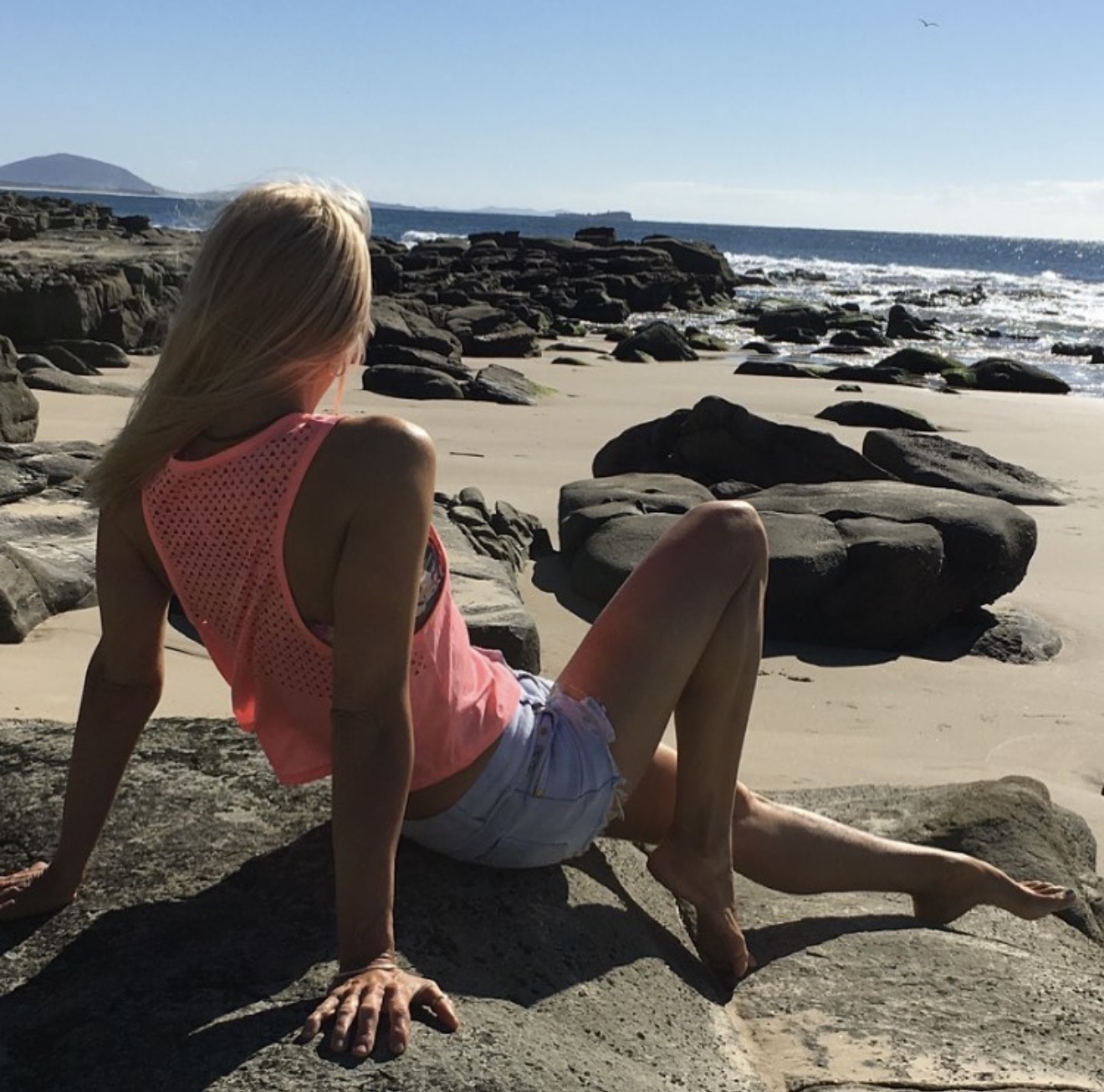 Kellie relaxing confidently on coastal rocks with ocean waves behind her